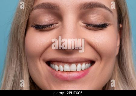 close-up of a woman with a snow-white Hollywood smile and closed eyes on a blue background Stock Photo