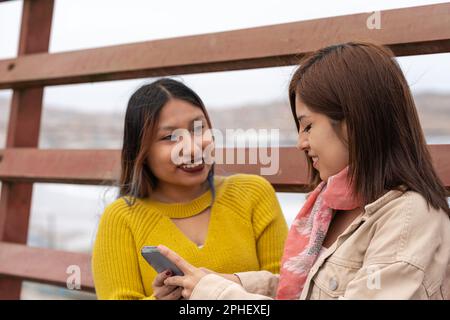 Two latin young friends using the mobile in the street Stock Photo