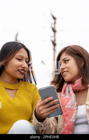 Vertical photo with copy space of two latin young friends using a mobile outdoors Stock Photo