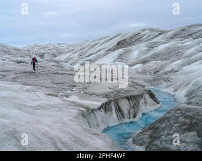 Tourists hiking on the ice. The brown sediment on the ice is created by the rapid melting of the ice. Landscape of the Greenland ice sheet near Kanger Stock Photo