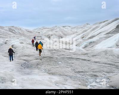 Tourists hiking on the ice. The brown sediment on the ice is created by the rapid melting of the ice. Landscape of the Greenland ice sheet near Kanger Stock Photo