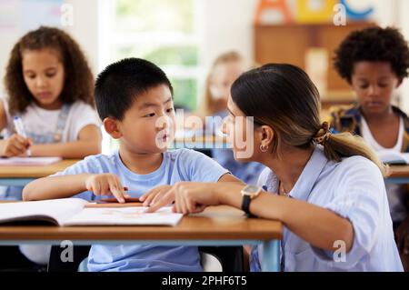 Teacher, learning and helping boy in classroom for knowledge, studying or assessment. Preschool, development and Asian kid or student with woman for Stock Photo