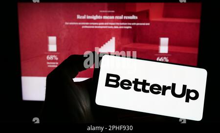 Person holding cellphone with logo of US coaching company BetterUp on screen in front of business webpage. Focus on phone display. Stock Photo