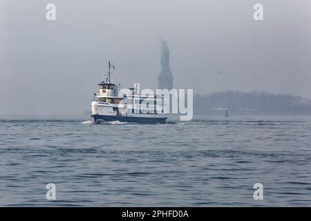 Commuters and tourists alike see the Statue of Liberty from ferries and tour boats in New York Harbor on a foggy February morning. Stock Photo