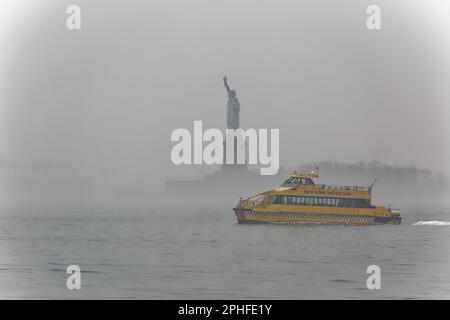 Commuters and tourists alike see the Statue of Liberty from ferries and tour boats in New York Harbor on a foggy February morning. Stock Photo