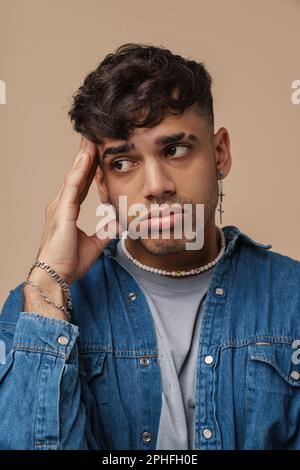 Young handsome stylish tired sad man touching his head and looking aside , while standing over isolated brown background Stock Photo