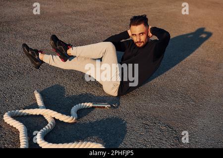 Doing abs. Man in sportswear have fitness day on the road at evening time Stock Photo