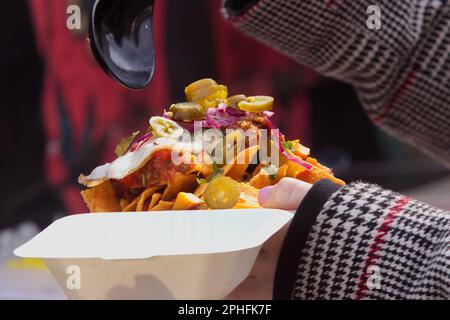 Woman holding plastic bowl of mexican food, egg, burrito, taco, nachos, jalapeno peppers and chili salsa sauce. Stock Photo