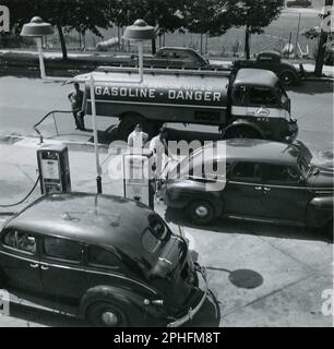 High level view of an Esso tank truck making a gasoline delivery while the station attendant fills the tanks of two customers, no location, NJ, 6/1945. (Photo by Standard Oil Company of New Jersey) Stock Photo