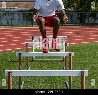 Front view of a high school boy jumping over track hurdles for strength and flexibility Stock Photo