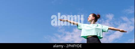 Young woman doing yoga against blue sky outdoors. Stock Photo