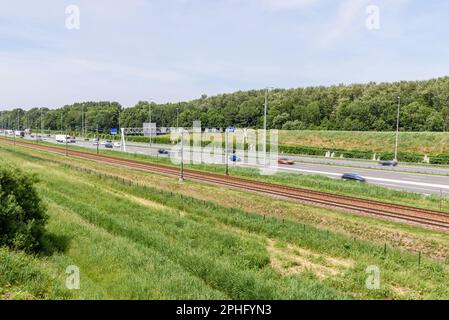 Motorway running parallel to railway tracks in the countryside of Netherlands on a sunny summer day Stock Photo