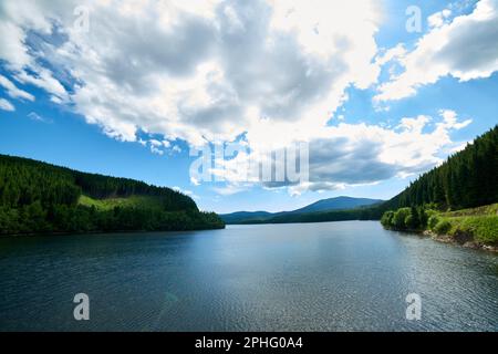 A tranquil lake is situated in an idyllic landscape, surrounded by lush, rolling hills, Carpathian mountains Stock Photo