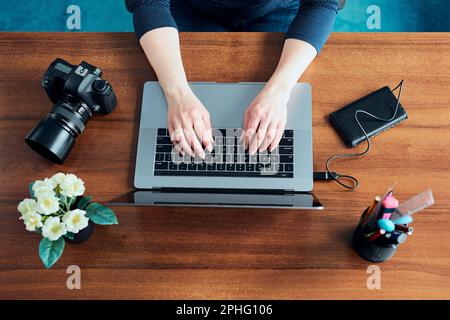 Female photographer working on photos on laptop and camera. Woman editing retouching browsing photos working as a freelancer sitting at desk Stock Photo