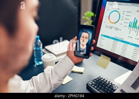 Man entrepreneur having business conversation, video chat on mobile phone. Businessman working with data, charts and graphs on computer screen. Man ho Stock Photo