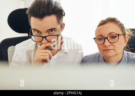 Two business people discussing financial data looking at computer screen. Entrepreneurs working hard sitting at computere screen in office. People hav Stock Photo