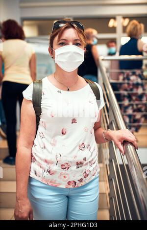 Woman going downstairs in public place inside wearing face mask to cover mouth and nose during pandemic coronavirus outbreak Stock Photo