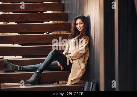 Cheerful brunette in black leggings sitting on wooden stairs and smiling Stock Photo
