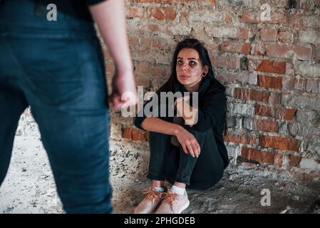 Violent man standing and threatens girl that sits on the floor with teddy bear in abandoned building Stock Photo