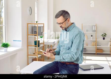Mature business man sitting on working desk in office and using his mobile phone Stock Photo