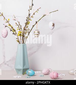 Colorful Easter eggs and spring twigs in vase against the background of marble wall Stock Photo