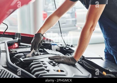 Man in uniform works with broken automobile. Conception of car service Stock Photo