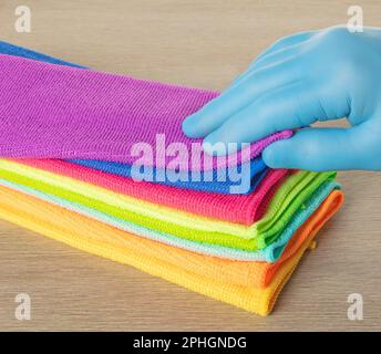 Hand in a blue glove selects a towel from a stack of bright microfiber towels for cleaning. Stock Photo