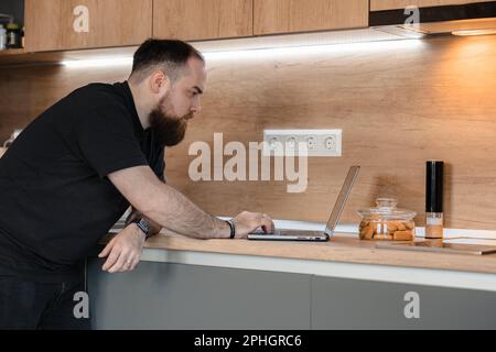 Bearded man working on his laptop in the comfort of his own kitchen Stock Photo