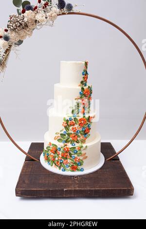 Beautiful four tiered wedding cake decorated with colorful icing flowers, surrounded by metal ring and bouquet. Stock Photo