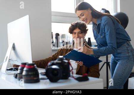 Female photo assistant with checklist and male photographer working together, planning photoshoot in studio Stock Photo