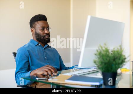 Serious african american male programmer working with new project on computer, sitting at desk in office, copy space Stock Photo