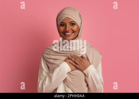 Gratitude Concept. Thankful muslim woman in hijab keeping hands on chest Stock Photo