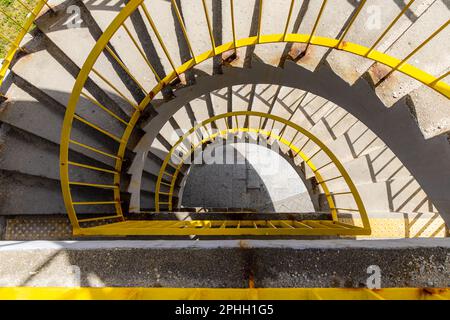 Top view of a concrete spiral staircase with yellow railings on a sunny morning Stock Photo