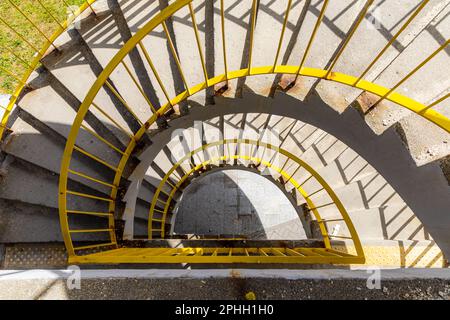 Top view of a concrete spiral staircase with yellow railings on a sunny morning Stock Photo