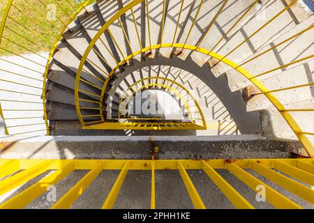 Top view of a concrete spiral staircase with yellow railings on a sunny morning Stock Photo