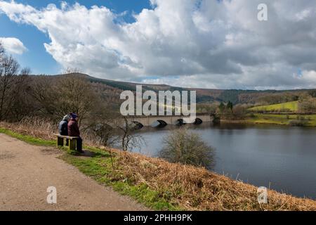 Ladybower reservoir in the Upper Derwent Valley, Peak District national park, on a sunny spring day. A couple enjoying the view near Ashopton Viaduct. Stock Photo