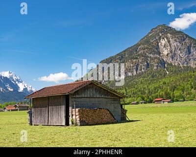Wooden barn on a sunlit meadow against the backdrop of the Ammergau Alps, Bavaria, Germany Stock Photo