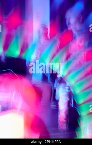Blurred and slow shutter speed of figures in bright saturated light at party Stock Photo
