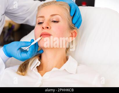 Cosmetologist applying marks on face of young female client Stock Photo