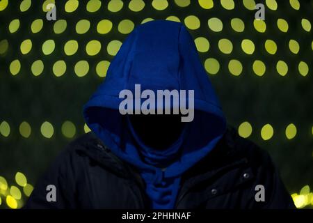 Faceless anonymous man wearing a hoodie while looking down, face not visible; Hacker wallpaper Stock Photo