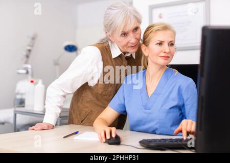 Interested elderly female client with cosmetologist looking at computer screen Stock Photo
