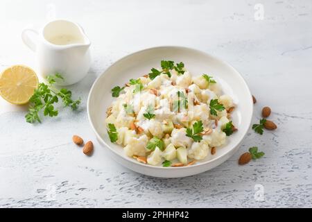 Cauliflower salad with apples, almonds, herbs and yogurt dressing on a light gray textured background. Healthy homemade diet food Stock Photo