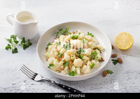 Cauliflower salad with apples, almonds, herbs and yogurt dressing on a light gray textured background. Healthy homemade diet food Stock Photo