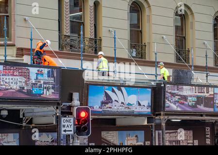 Smiling happy construction workers standing on the top of a gantry hoarding wrapped around a building in central Sydney, New South Wales, Australia Stock Photo