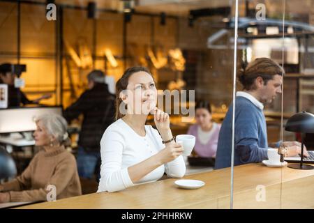 Portrait of focused female surfing Internet on notebook while drinking tea or coffee in cafeteria Stock Photo