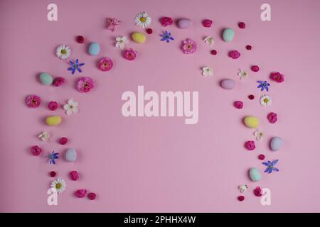Easter concept. Top view of colorful easter eggs spring flowers on pink background with blank space. Stock Photo