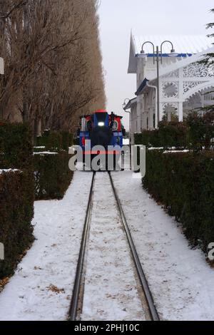 Colorful train seen behind railway under snow. Train parked and nostalgic vintage train station Stock Photo