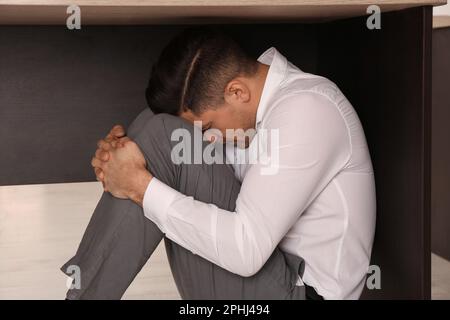 Scared man hiding under office desk during earthquake Stock Photo