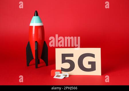 Internet concept. Paper with phrase 5G, toy rocket and SIM cards on red background Stock Photo