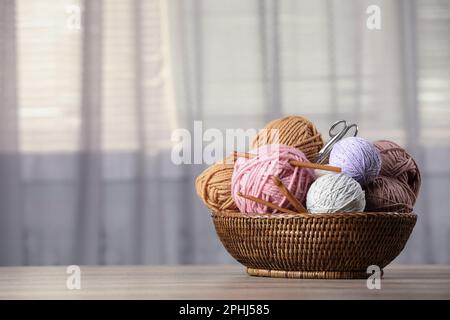 Wicker basket with clews of colorful knitting threads, crochet hooks and scissors on wooden table indoors. Space for text Stock Photo